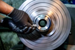 Disque de métal en rotation sur un tour, guidé par une main gantée