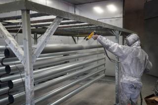 Opérateur en combinaison appliquant une peinture poudre sur des tubes métalliques